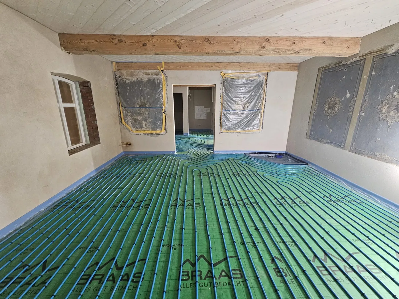 Raumübersicht mit Holzbalken und verlegter getackerter Fußbodenheizung